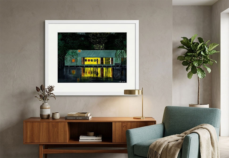 Painting of a rustic cabin with glowing yellow windows and green mossy walls, displayed on a textured gray wall above a wooden console table in a modern living room setting.
